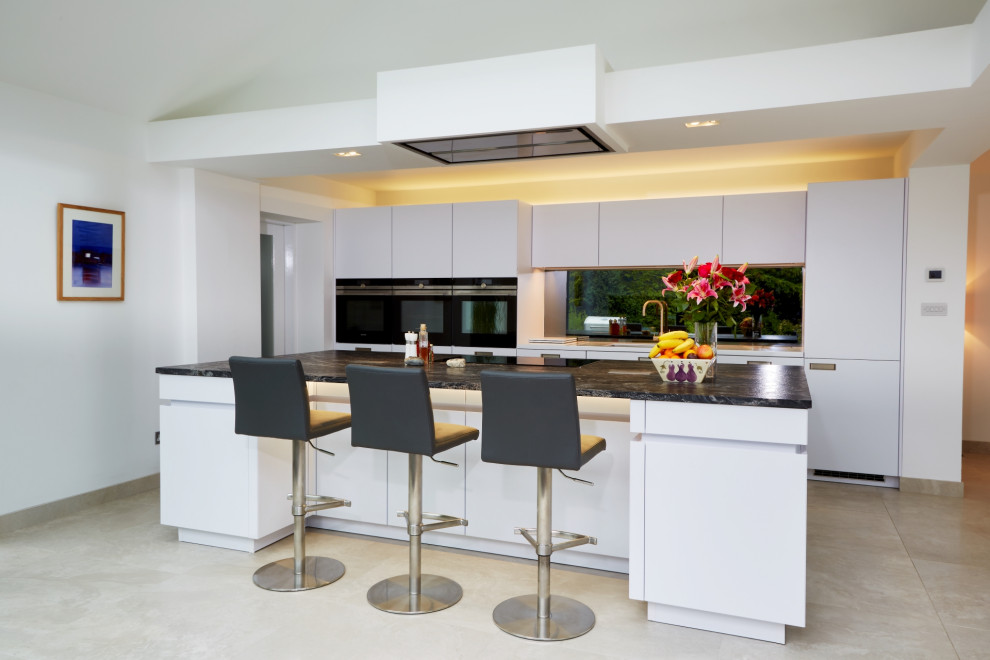 Design ideas for a mid-sized contemporary single-wall eat-in kitchen in Other with flat-panel cabinets, white cabinets, granite benchtops, metallic splashback, mirror splashback, panelled appliances, with island and blue benchtop.