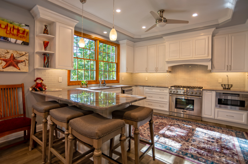 Large traditional u-shaped eat-in kitchen in Philadelphia with an undermount sink, raised-panel cabinets, white cabinets, granite benchtops, yellow splashback, glass tile splashback, stainless steel appliances, medium hardwood floors, a peninsula, brown floor and grey benchtop.