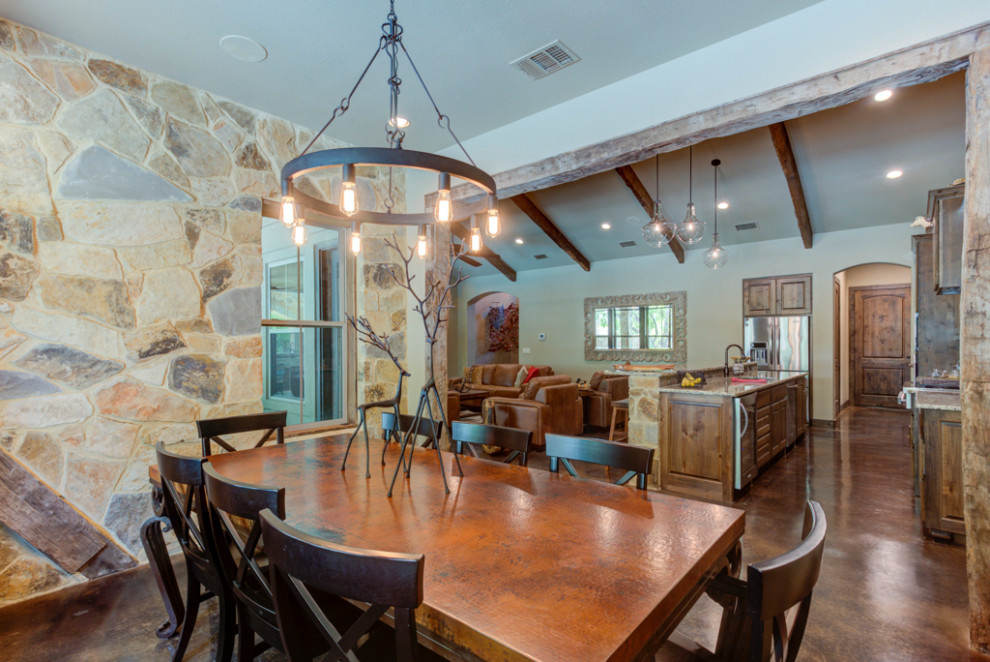 This is an example of a mid-sized country kitchen/dining combo in Austin with brown walls, concrete floors, a standard fireplace, a stone fireplace surround, black floor, wood and wood walls.