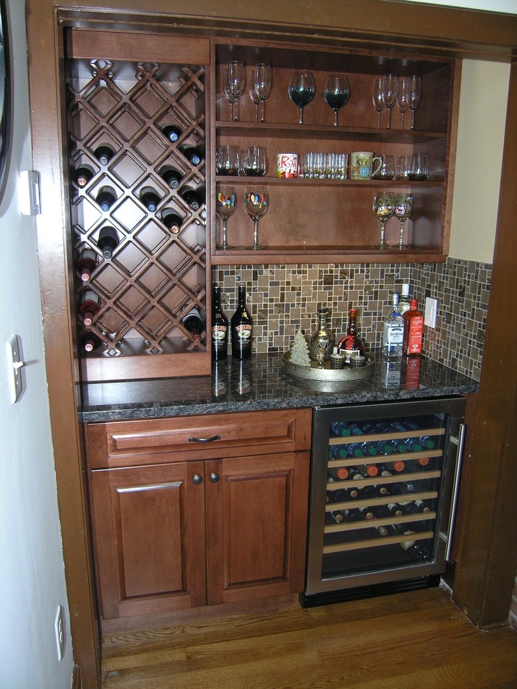 Photo of a small traditional single-wall wet bar in Tampa with no sink, medium wood cabinets, granite benchtops, brown splashback, porcelain splashback, medium hardwood floors, brown floor and recessed-panel cabinets.