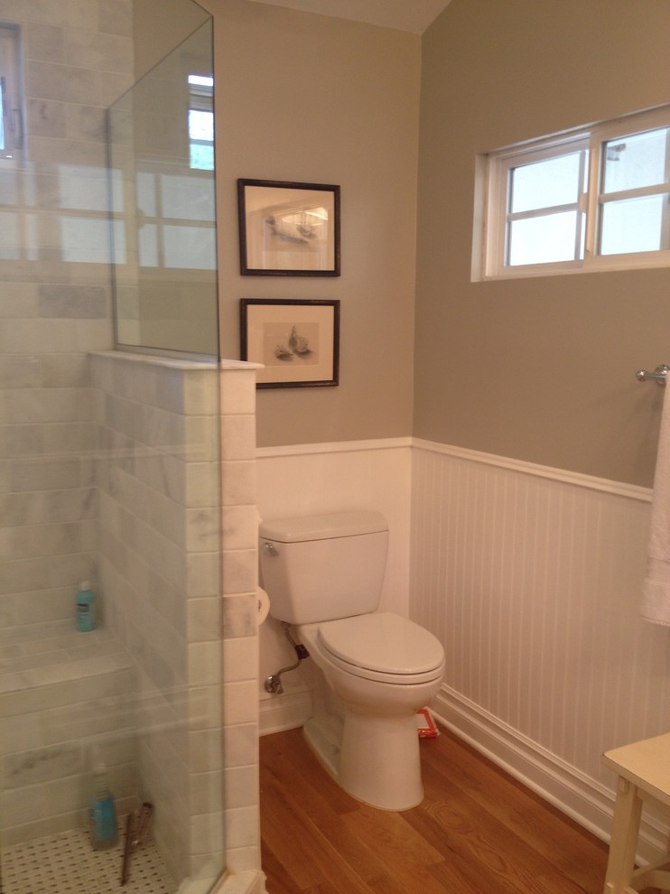Inspiration for a mid-sized traditional 3/4 bathroom in Orange County with recessed-panel cabinets, white cabinets, a corner shower, a two-piece toilet, gray tile, beige walls, medium hardwood floors, an undermount sink and marble benchtops.
