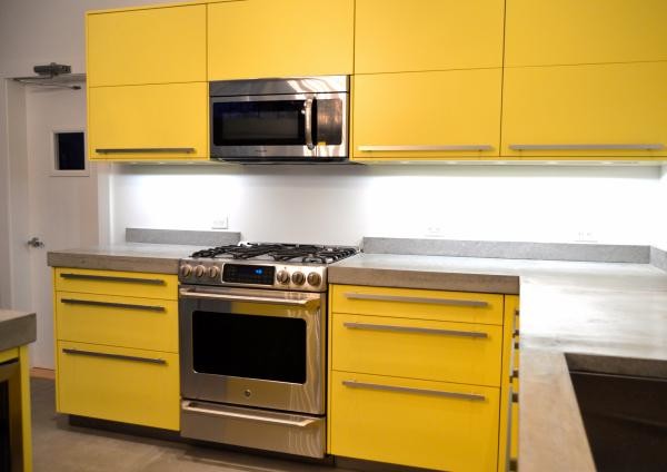 This is an example of a mid-sized modern l-shaped eat-in kitchen in New York with a drop-in sink, flat-panel cabinets, yellow cabinets, solid surface benchtops, coloured appliances, ceramic floors and with island.