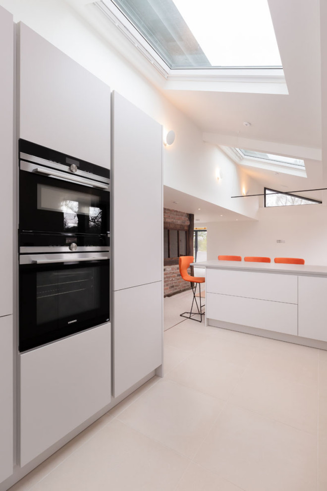 Design ideas for a small modern galley eat-in kitchen in Cheshire with a double-bowl sink, flat-panel cabinets, white cabinets, quartzite benchtops, engineered quartz splashback, black appliances, ceramic floors, beige floor, white benchtop and exposed beam.