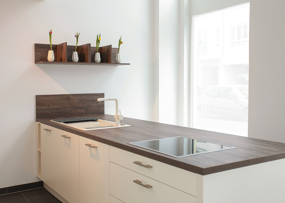 Contemporary kitchen in Leipzig with a drop-in sink, flat-panel cabinets, white cabinets, wood benchtops and a peninsula.