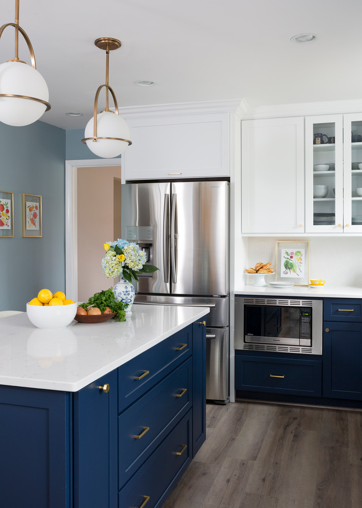 This is an example of a mid-sized transitional l-shaped kitchen in Other with a farmhouse sink, shaker cabinets, blue cabinets, quartz benchtops, white splashback, with island, medium hardwood floors and brown floor.