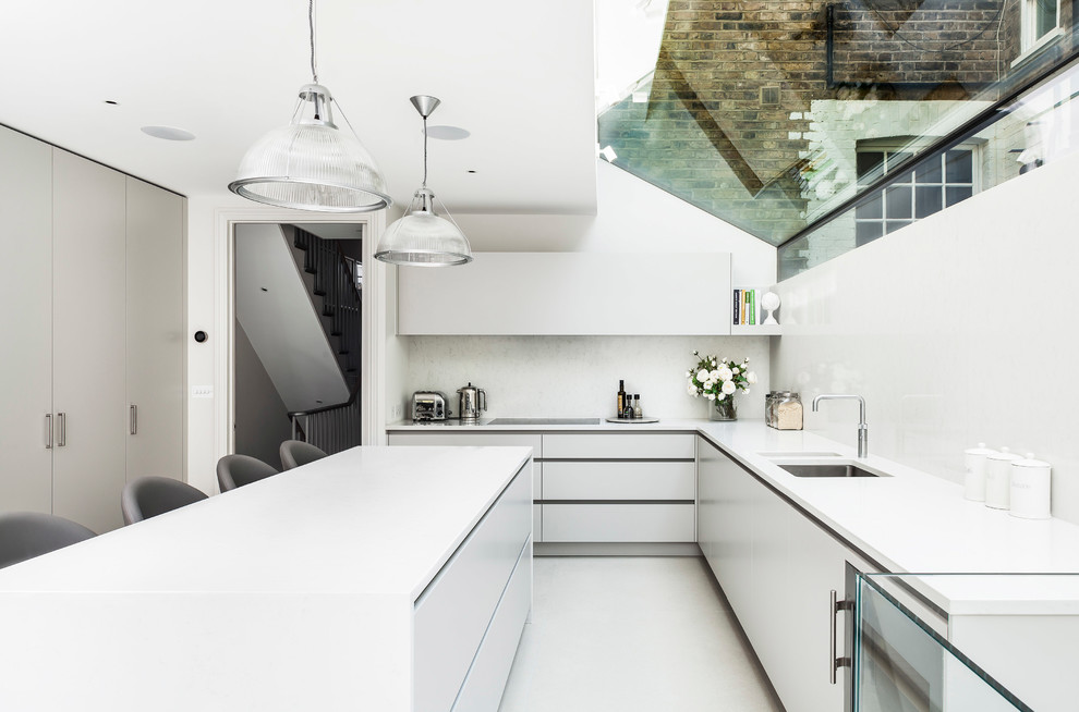 Contemporary open plan kitchen in London with an integrated sink, flat-panel cabinets, white cabinets, solid surface benchtops, white splashback, stainless steel appliances, ceramic floors and with island.