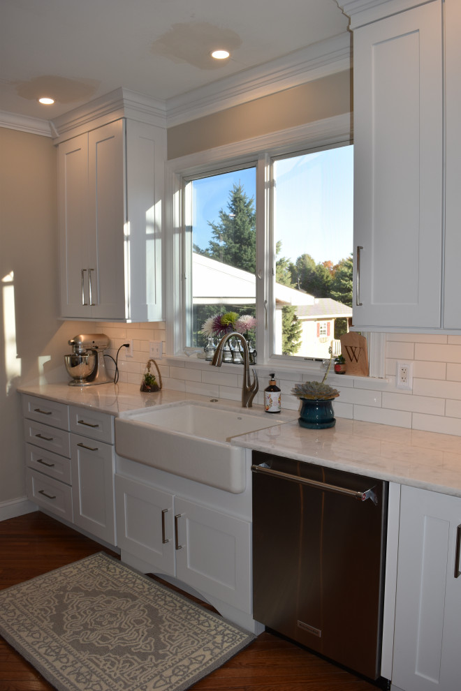 Klassisk inredning av ett stort vit vitt kök, med en rustik diskho, luckor med infälld panel, vita skåp, bänkskiva i kvartsit, vitt stänkskydd, stänkskydd i tunnelbanekakel, rostfria vitvaror, mellanmörkt trägolv, en köksö och brunt golv