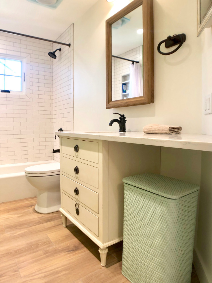 Small country kids bathroom in Philadelphia with furniture-like cabinets, white cabinets, an alcove tub, a shower/bathtub combo, a two-piece toilet, white tile, ceramic tile, white walls, wood-look tile, an undermount sink, brown floor, a shower curtain, white benchtops, limestone benchtops, a niche, a single vanity, a freestanding vanity and vaulted.