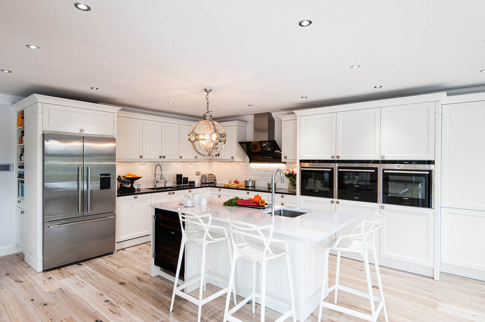 This is an example of a large traditional l-shaped open plan kitchen in London with an undermount sink, recessed-panel cabinets, white cabinets, white splashback, subway tile splashback, stainless steel appliances, light hardwood floors, with island and quartzite benchtops.