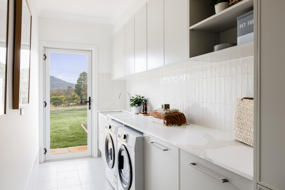 This is an example of a large contemporary single-wall dedicated laundry room in Wollongong with a farmhouse sink, white splashback, subway tile splashback, white walls, ceramic floors, a side-by-side washer and dryer and grey floor.