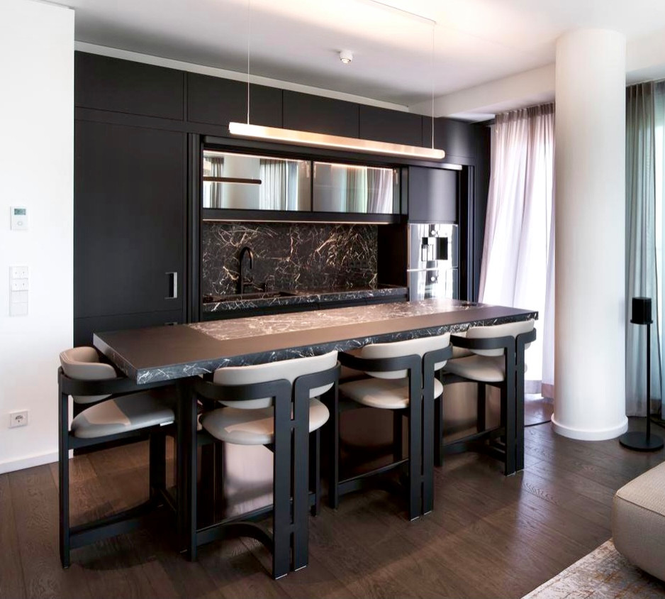 This is an example of a contemporary home bar in Frankfurt with an integrated sink, flat-panel cabinets, black cabinets, marble benchtops, black splashback, marble splashback, medium hardwood floors, brown floor and black benchtop.