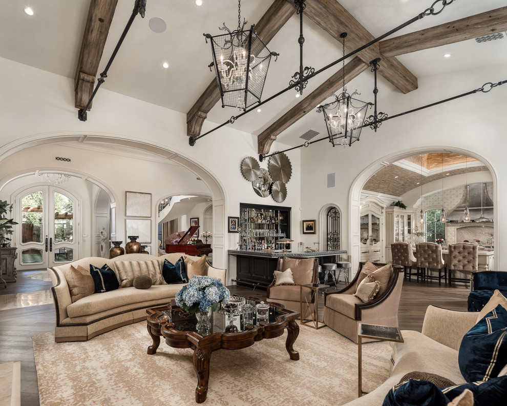 Expansive traditional open concept family room in Phoenix with a home bar, white walls, medium hardwood floors, a standard fireplace, a stone fireplace surround, a wall-mounted tv and brown floor.