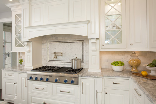 Transitional white kitchen with raised-panel cabinets, brushed nickel pulls and knobs, marble countertop, pot filler, and a stainless gas range.