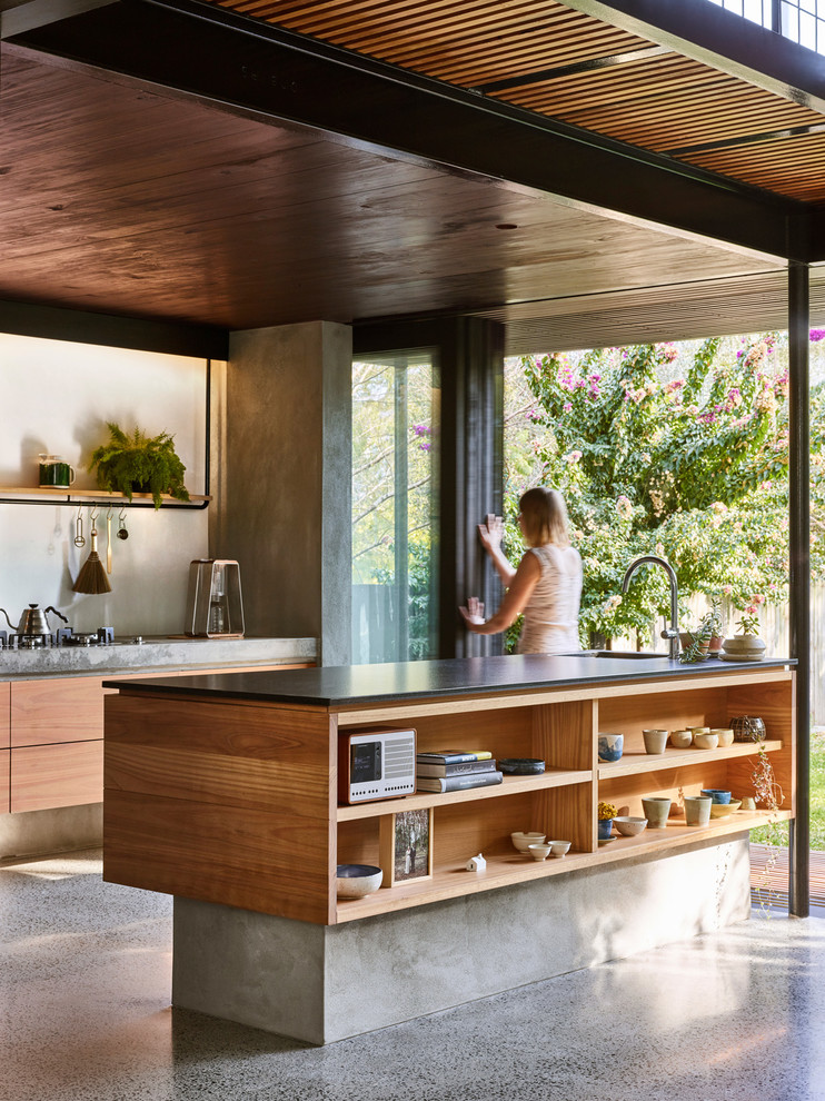 This is an example of a small modern galley kitchen pantry in Brisbane with an undermount sink, flat-panel cabinets, light wood cabinets, granite benchtops, white splashback, black appliances, concrete floors, with island and grey floor.