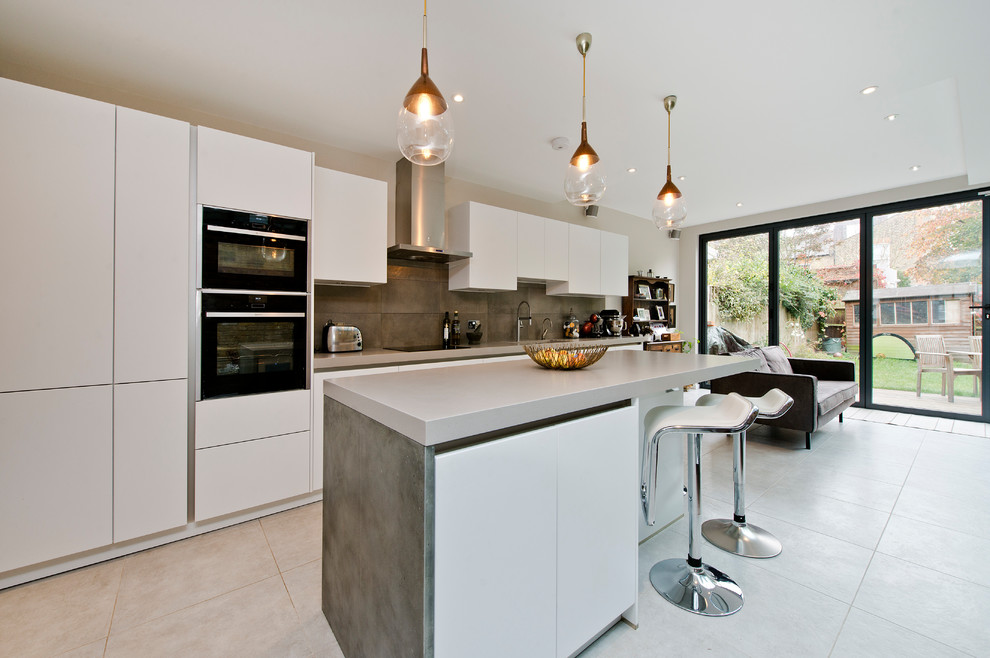 Photo of a mid-sized contemporary l-shaped eat-in kitchen in London with an integrated sink, flat-panel cabinets, white cabinets, solid surface benchtops, metallic splashback, ceramic splashback, black appliances and with island.