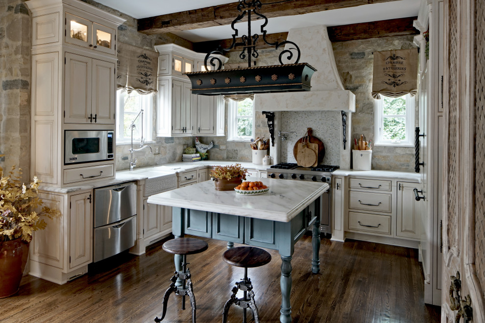 Example of a large french country u-shaped dark wood floor, brown floor and exposed beam open concept kitchen design in Chicago with a farmhouse sink, raised-panel cabinets, beige cabinets, marble countertops, multicolored backsplash, stone slab backsplash, stainless steel appliances, an island and white countertops