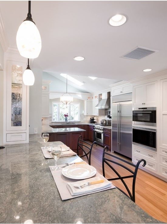 This is an example of an expansive traditional l-shaped eat-in kitchen in Providence with a double-bowl sink, beaded inset cabinets, beige cabinets, granite benchtops, beige splashback, marble splashback, stainless steel appliances, bamboo floors, multiple islands and brown floor.