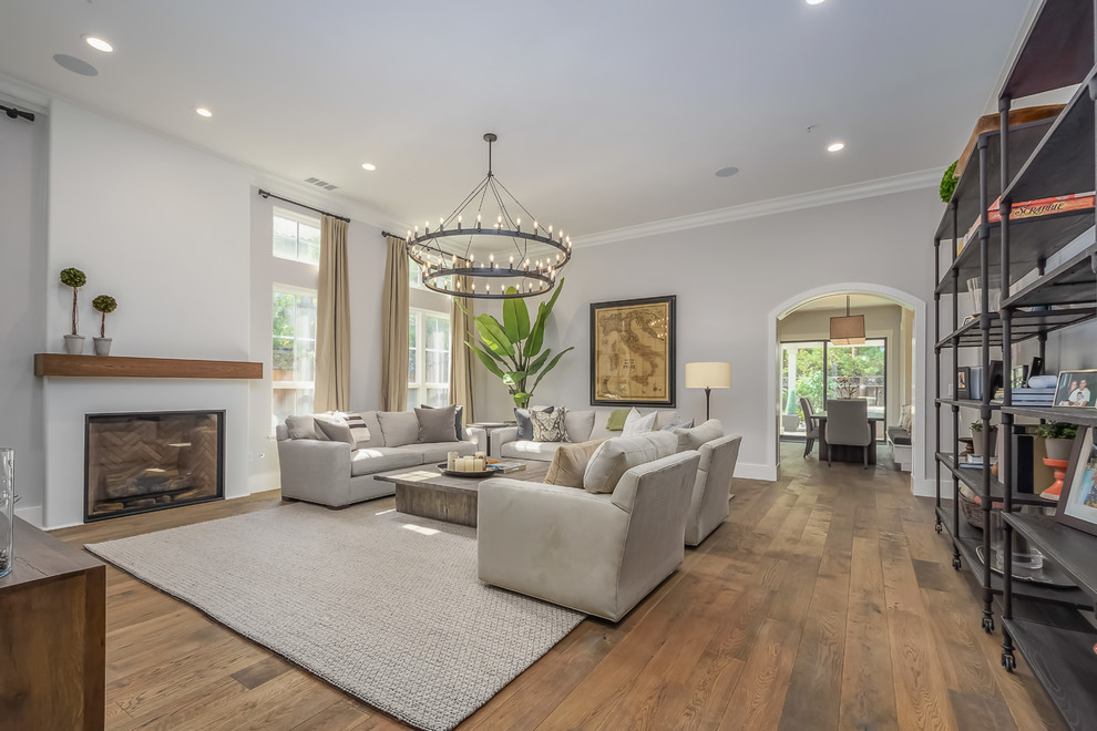 Large contemporary enclosed living room in San Francisco with grey walls, medium hardwood floors, a standard fireplace, a plaster fireplace surround, brown floor and a wall-mounted tv.