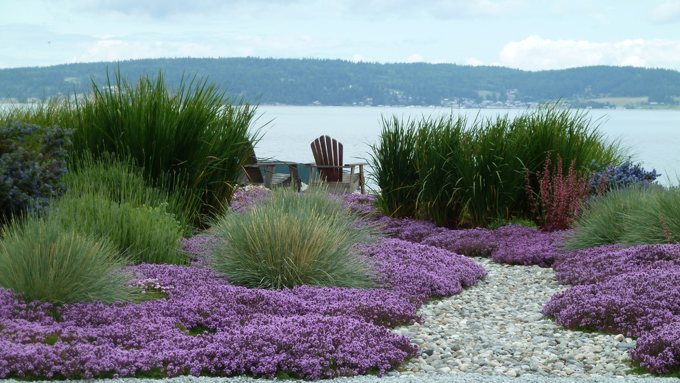 Small beach style backyard full sun xeriscape in Seattle with with flowerbed and river rock for summer.