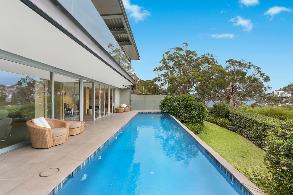 Inspiration for a large contemporary backyard custom-shaped lap pool in Sydney with natural stone pavers.