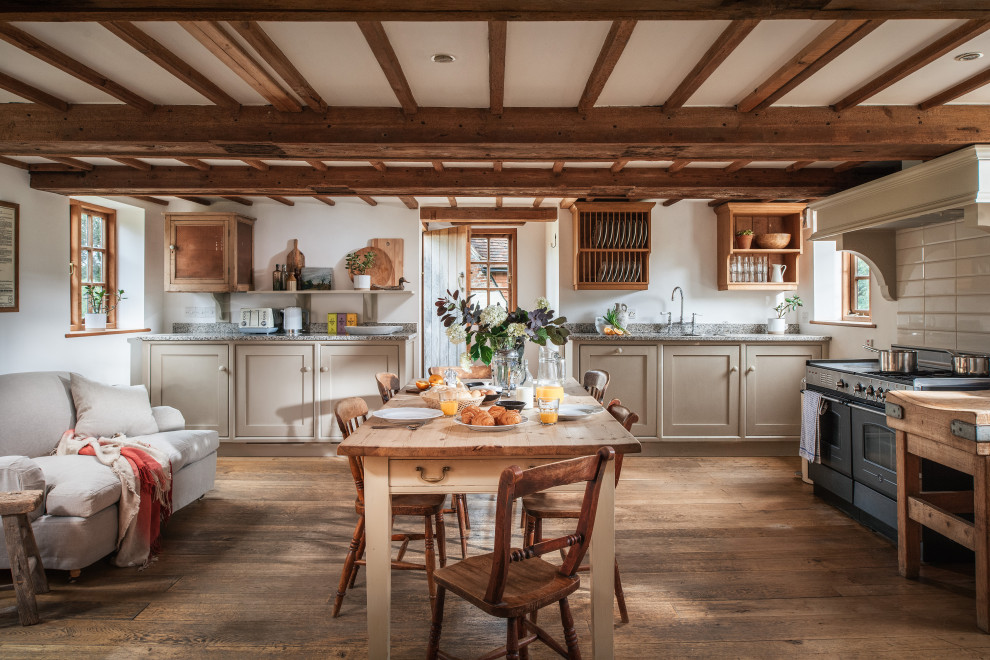 Large country kitchen/diner in Sussex with a built-in sink, recessed-panel cabinets, beige cabinets, granite worktops, black appliances, medium hardwood flooring, an island, brown floors, grey worktops and exposed beams.