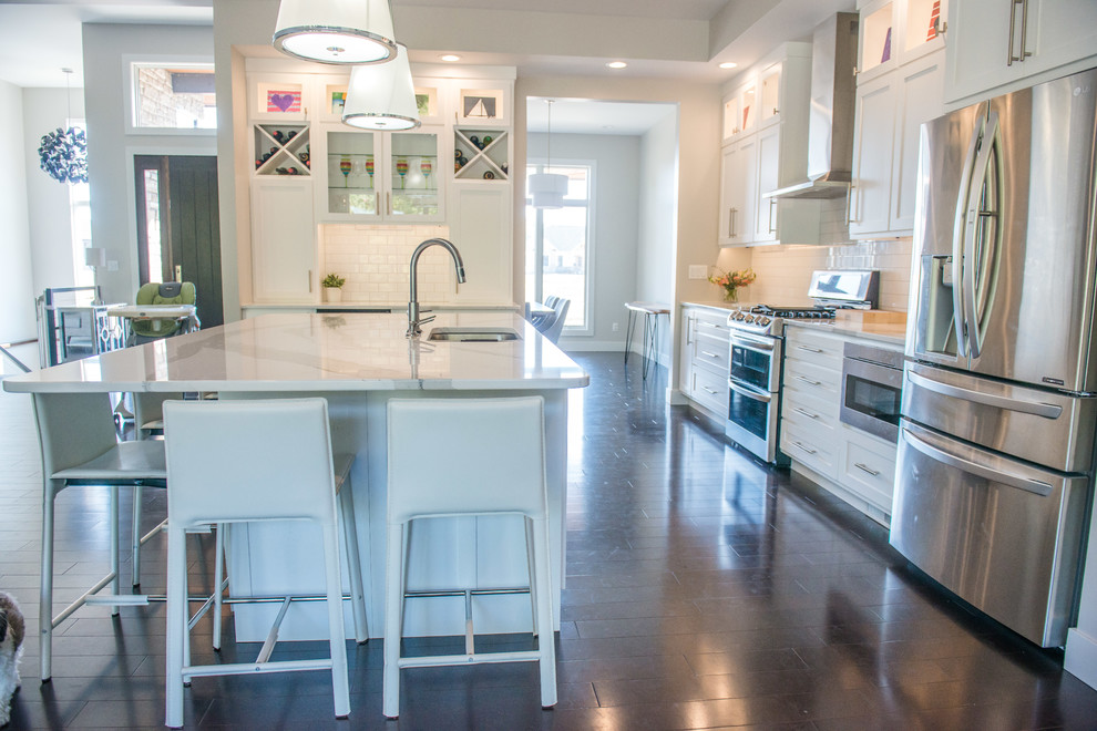 Example of a huge transitional l-shaped dark wood floor and brown floor open concept kitchen design in Chicago with a double-bowl sink, shaker cabinets, white cabinets, quartz countertops, white backsplash, ceramic backsplash, stainless steel appliances and an island