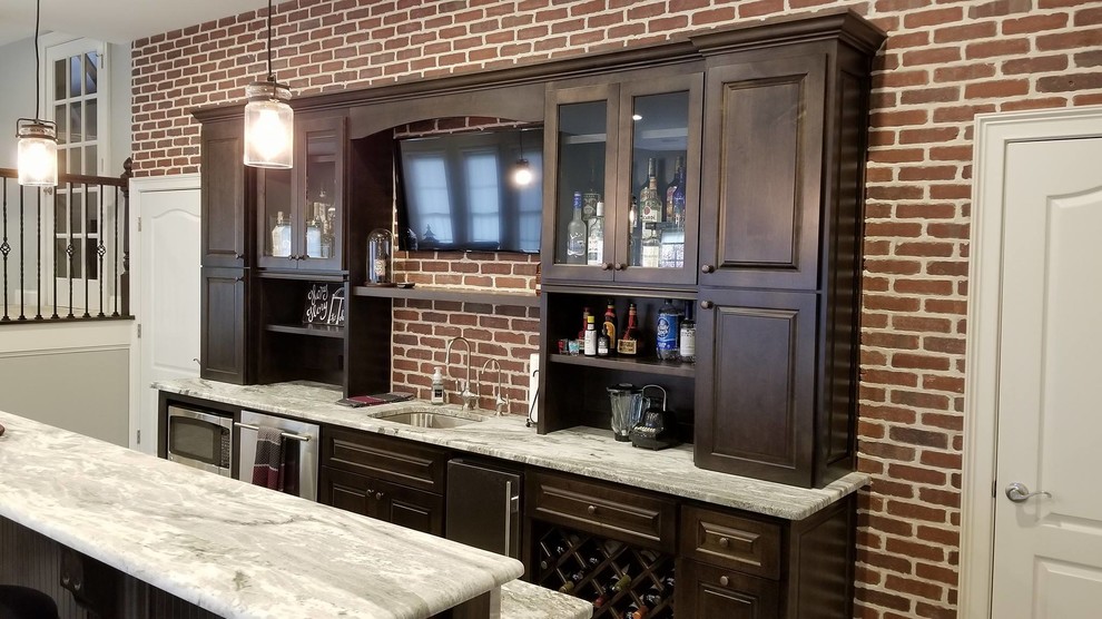 Large transitional galley seated home bar in Atlanta with an undermount sink, raised-panel cabinets, dark wood cabinets, red splashback, brick splashback, porcelain floors and brown floor.