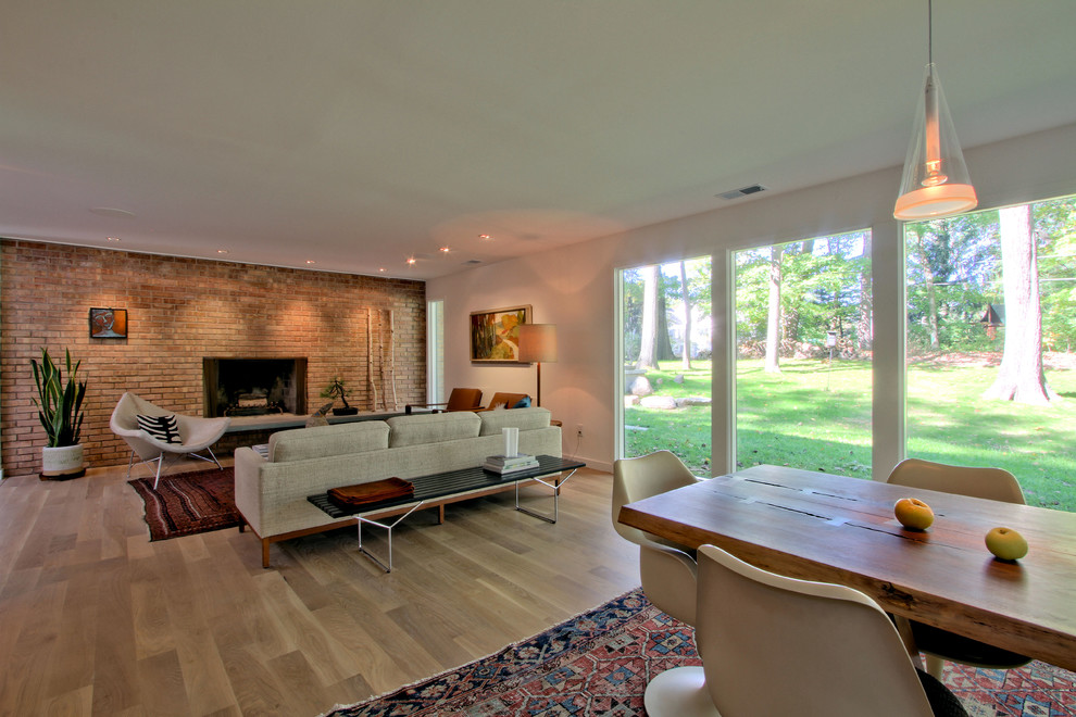 Mid-sized midcentury open concept living room in Indianapolis with white walls, light hardwood floors, a standard fireplace, a brick fireplace surround, no tv and beige floor.