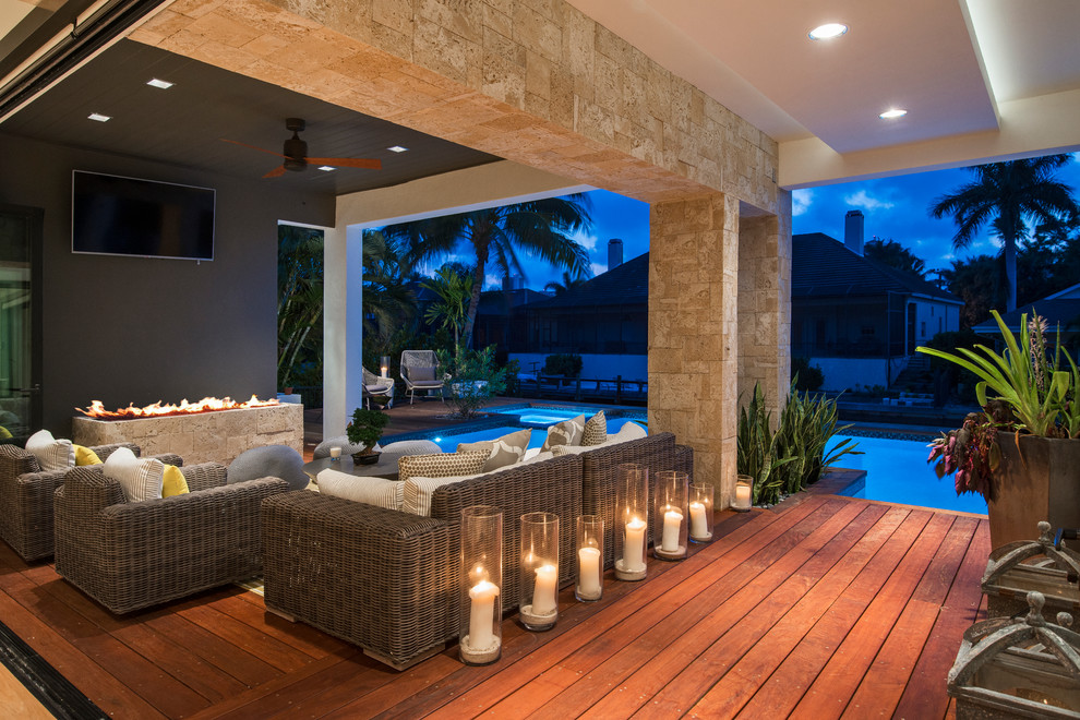 Photo of a large transitional backyard deck in Miami with a roof extension and a fire feature.
