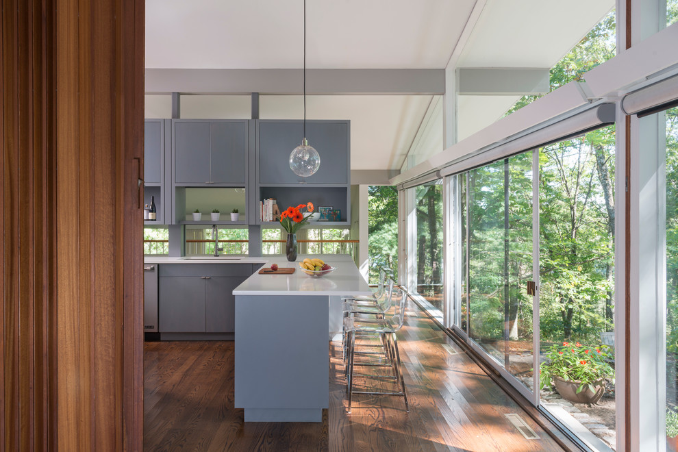 This is an example of a midcentury l-shaped eat-in kitchen in Boston with a single-bowl sink, grey cabinets, quartz benchtops, white splashback, mosaic tile splashback, stainless steel appliances, dark hardwood floors, flat-panel cabinets and with island.