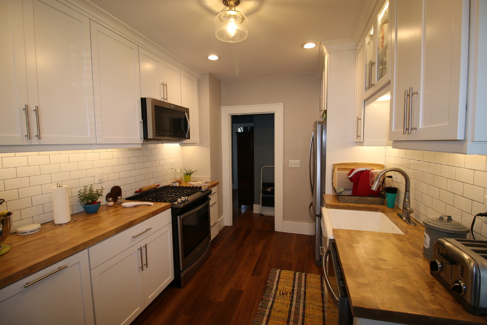 Design ideas for a small country galley separate kitchen in Little Rock with a farmhouse sink, shaker cabinets, white cabinets, wood benchtops, white splashback, subway tile splashback, stainless steel appliances, vinyl floors, brown floor and brown benchtop.