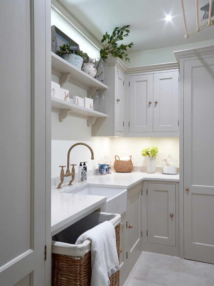 Photo of a medium sized classic l-shaped utility room in London with a belfast sink, shaker cabinets, quartz worktops, white splashback, metro tiled splashback, stainless steel appliances, light hardwood flooring, an island, beige cabinets, beige floors and white worktops.