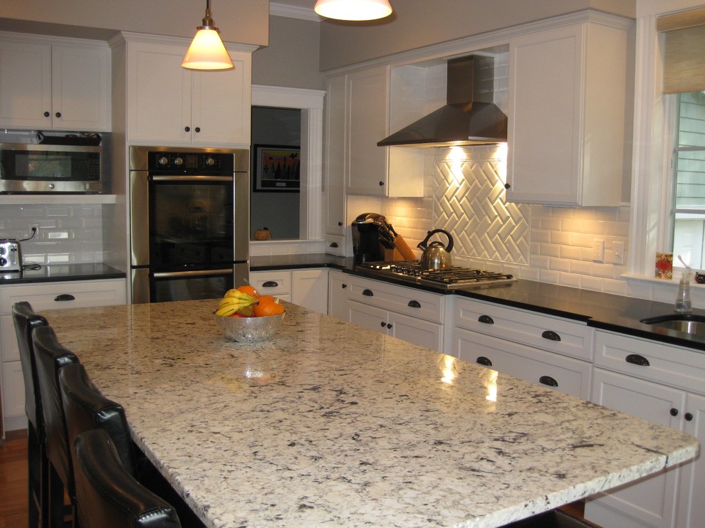 Inspiration for a transitional l-shaped medium tone wood floor eat-in kitchen remodel in Boston with an undermount sink, shaker cabinets, white cabinets, granite countertops, white backsplash, ceramic backsplash, stainless steel appliances, an island and black countertops