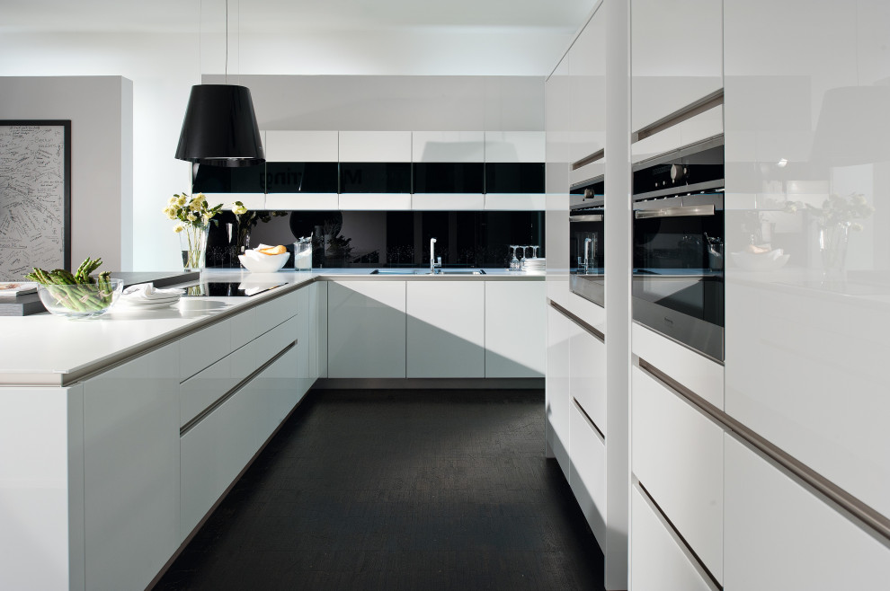 Photo of a mid-sized modern l-shaped eat-in kitchen in Toronto with an undermount sink, flat-panel cabinets, white cabinets, quartz benchtops, black splashback, glass sheet splashback, stainless steel appliances, ceramic floors, a peninsula, black floor and white benchtop.