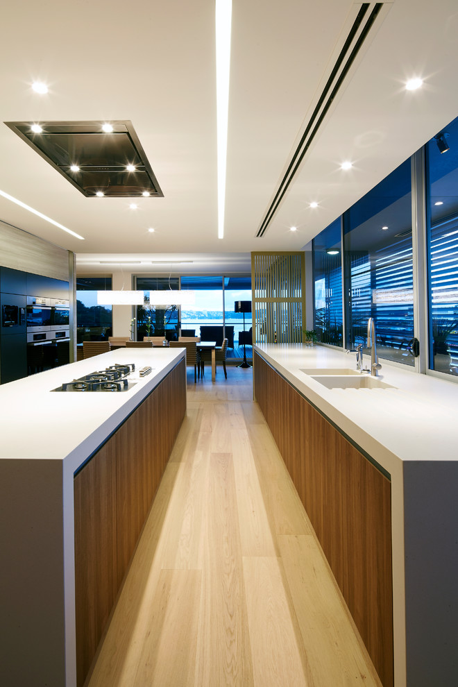 Photo of a modern galley kitchen in Sydney with an integrated sink, flat-panel cabinets, dark wood cabinets, concrete benchtops, window splashback, black appliances, light hardwood floors, with island, beige floor and grey benchtop.