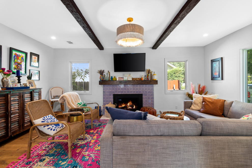 Mediterranean living room in Sacramento with grey walls, medium hardwood flooring, a standard fireplace, a tiled fireplace surround, brown floors and exposed beams.