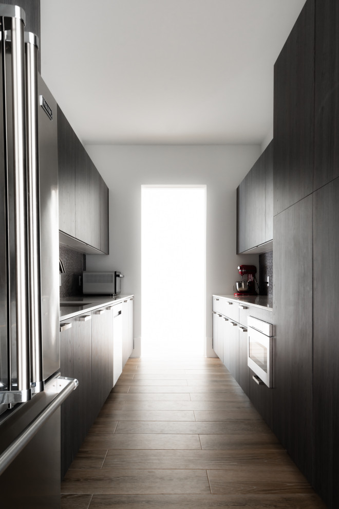 This is an example of a mid-sized contemporary galley kitchen pantry in Houston with flat-panel cabinets, grey splashback, grey benchtop, black cabinets, brick splashback, stainless steel appliances, with island, brown floor, an undermount sink and medium hardwood floors.