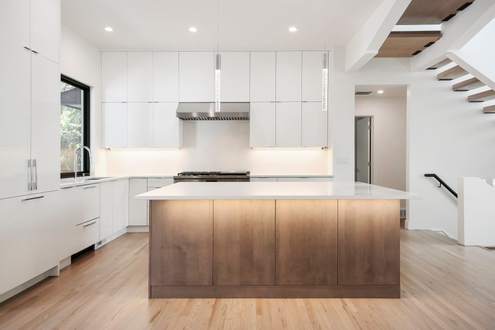 Photo of a large modern l-shaped kitchen/diner in Denver with a double-bowl sink, flat-panel cabinets, white cabinets, white appliances, light hardwood flooring, an island, brown floors and white worktops.