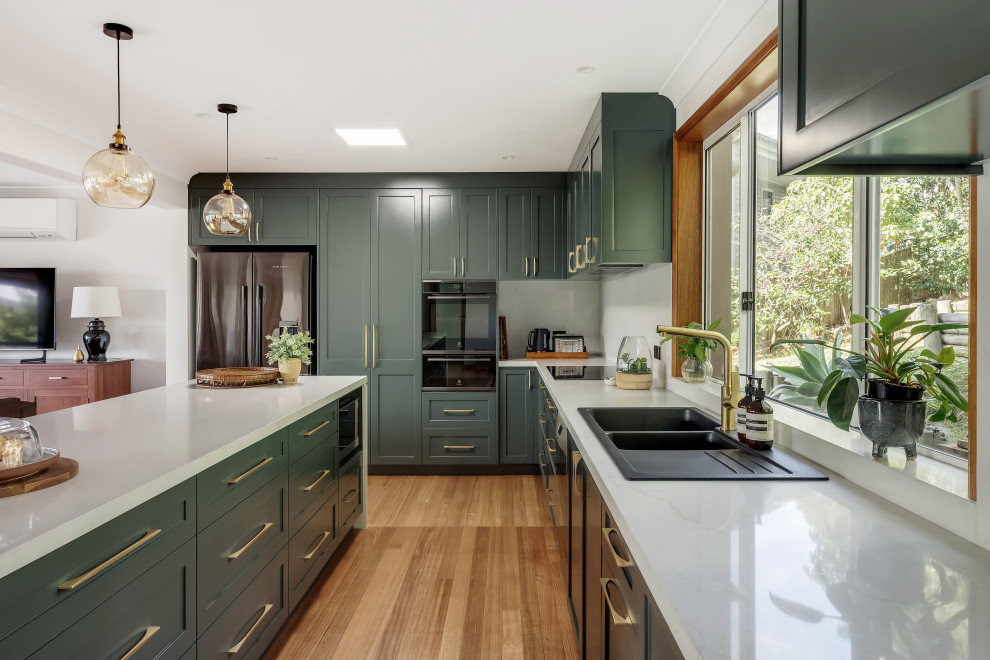 Eat-in kitchen - large transitional l-shaped medium tone wood floor and multicolored floor eat-in kitchen idea in Sydney with a drop-in sink, shaker cabinets, green cabinets, quartz countertops, white backsplash, quartz backsplash, black appliances, an island and white countertops