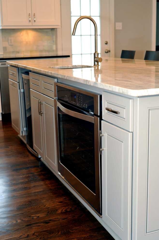 Mid-sized transitional l-shaped medium tone wood floor open concept kitchen photo in Atlanta with a double-bowl sink, white cabinets, quartzite countertops, white backsplash, stainless steel appliances and an island