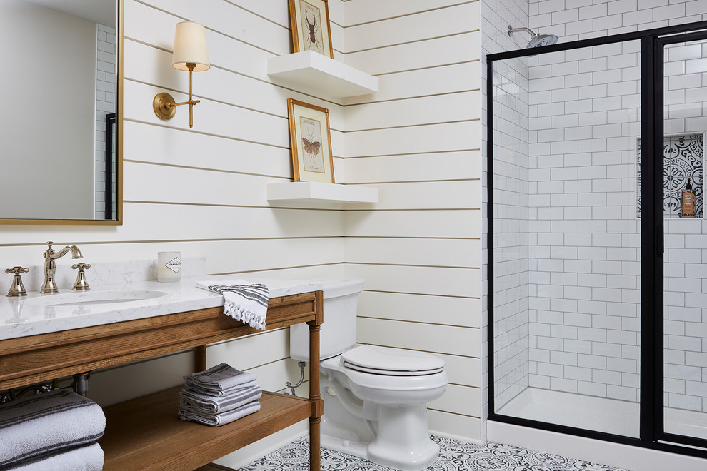 This is an example of a mid-sized country 3/4 bathroom in Minneapolis with an alcove shower, a two-piece toilet, porcelain tile, white walls, cement tiles, an undermount sink, marble benchtops, a hinged shower door, white benchtops, medium wood cabinets, white tile and multi-coloured floor.