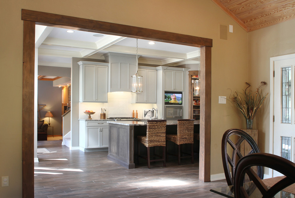 Example of a huge transitional l-shaped porcelain tile eat-in kitchen design with a farmhouse sink, recessed-panel cabinets, gray cabinets, granite countertops, white backsplash, ceramic backsplash, stainless steel appliances and an island