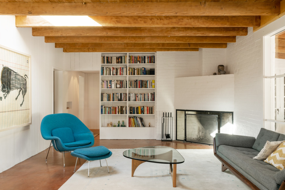 This is an example of a living room in Phoenix with white walls, concrete floors, a corner fireplace, a brick fireplace surround, brown floor, exposed beam, brick walls and planked wall panelling.