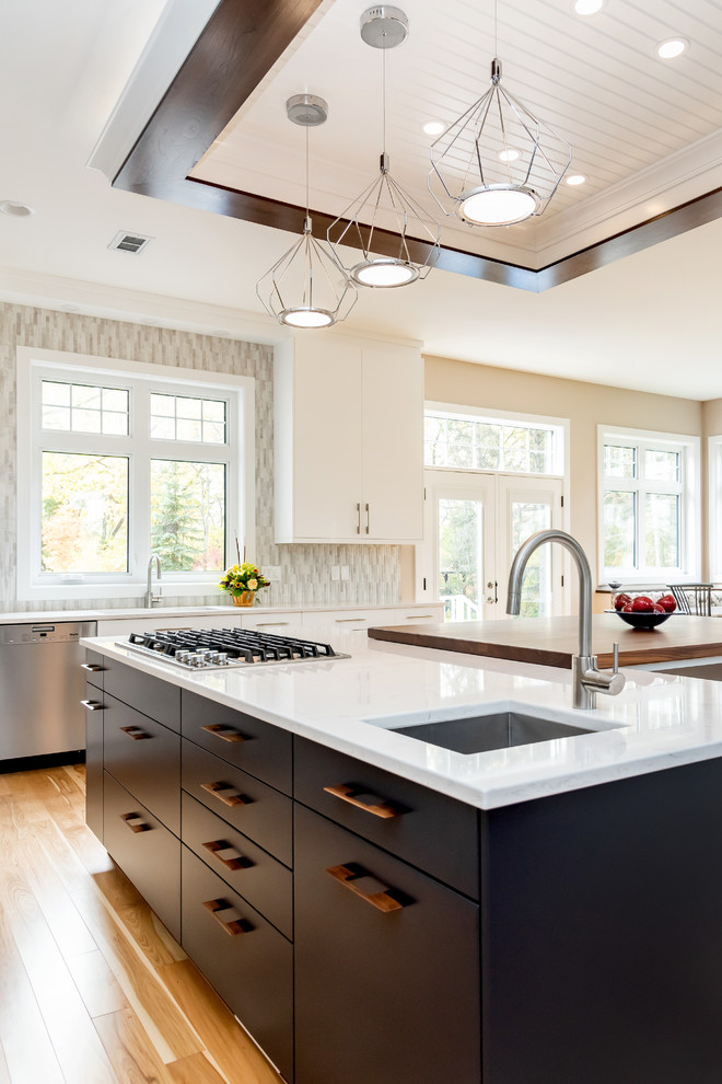 Large transitional l-shaped light wood floor and beige floor kitchen pantry photo with a double-bowl sink, flat-panel cabinets, white cabinets, quartz countertops, gray backsplash, cement tile backsplash, stainless steel appliances, an island and white countertops