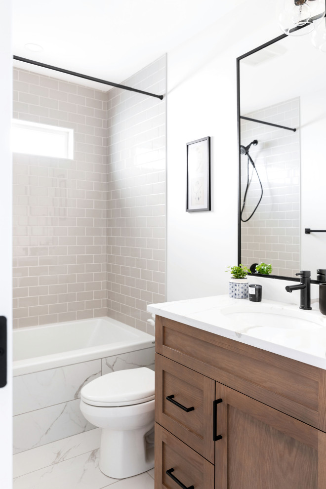 This is an example of a large contemporary bathroom in Calgary with shaker cabinets, beige cabinets, a drop-in tub, a shower/bathtub combo, a one-piece toilet, beige tile, ceramic tile, white walls, marble floors, an undermount sink, marble benchtops, white floor, a shower curtain, white benchtops, a single vanity and a built-in vanity.