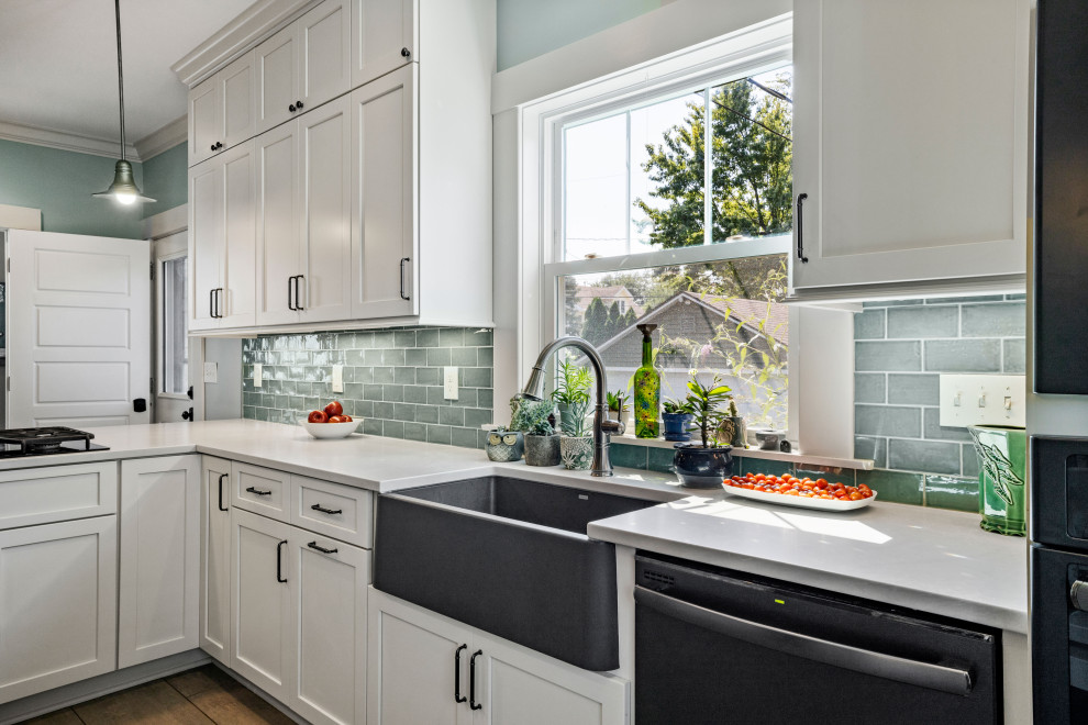 Photo of a mid-sized traditional l-shaped eat-in kitchen in Columbus with a farmhouse sink, shaker cabinets, white cabinets, quartz benchtops, green splashback, cement tile splashback, black appliances, porcelain floors, a peninsula, grey floor and white benchtop.