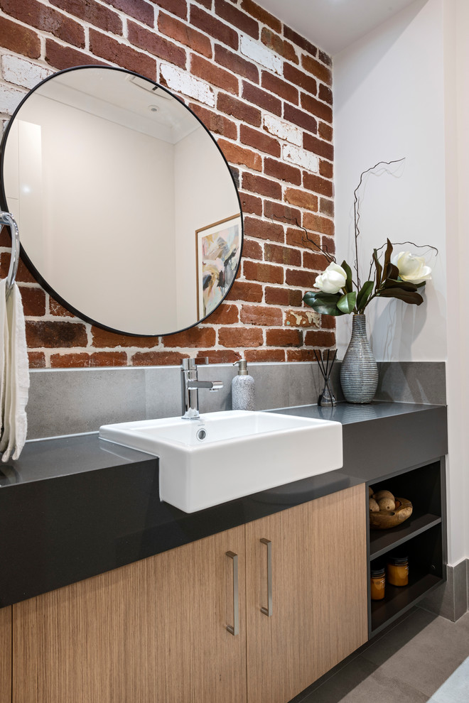 Photo of a mid-sized contemporary powder room in Perth with medium wood cabinets, gray tile, orange walls, a drop-in sink, solid surface benchtops, black benchtops, ceramic tile, ceramic floors and grey floor.