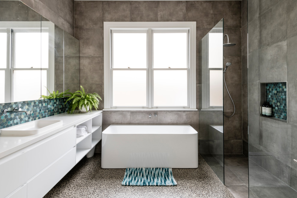 Пример оригинального дизайна: большая главная, серо-белая ванная комната: освещение в современном стиле с фасадами в стиле шейкер, белыми фасадами, отдельно стоящей ванной, угловым душем, унитазом-моноблоком, синей плиткой, керамической плиткой, бежевыми стенами, полом из цементной плитки, накладной раковиной, столешницей из искусственного кварца, серым полом, открытым душем, белой столешницей, тумбой под две раковины, встроенной тумбой и потолком с обоями