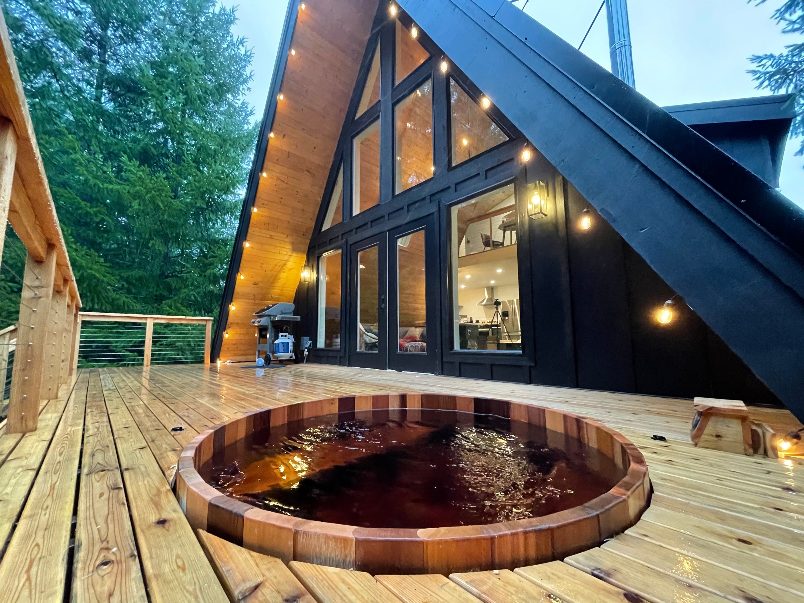 A spacious deck with a built-in hot tub, perfect for outdoor gatherings and relaxation. The deck features natural wood flooring and railings, blending harmoniously with the surrounding forest.