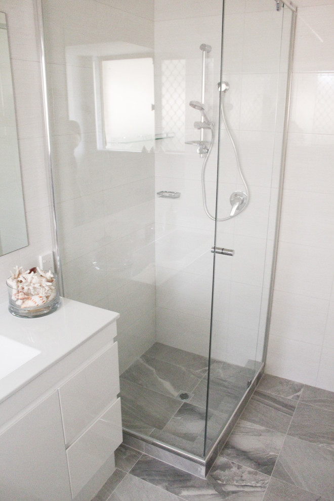 This is an example of a small modern kids bathroom in Perth with flat-panel cabinets, white cabinets, a drop-in tub, a corner shower, white tile, porcelain tile, grey walls, porcelain floors, an integrated sink, solid surface benchtops, grey floor, a hinged shower door and white benchtops.